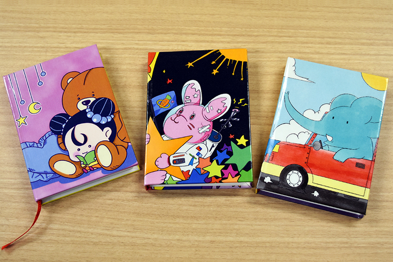 入選したイラストを使って、オリジナルミニブックを製本してもらいました!
(写真左)スクサモソーン チュティモンさんの作品「好きなもの(この子にとっては可愛いもの)に囲まれながら本を読もうというテーマで描きました」
(写真中央)倉持 楓さんの作品「幼少期に情報量の多い絵本を読んでワクワクした記憶があったので、細かいモチーフをたくさん置いて、ごちゃっとさせました」
(写真右)キン セイさんの作品「子供向けの象の世界旅行の物語をイメージして描きました」